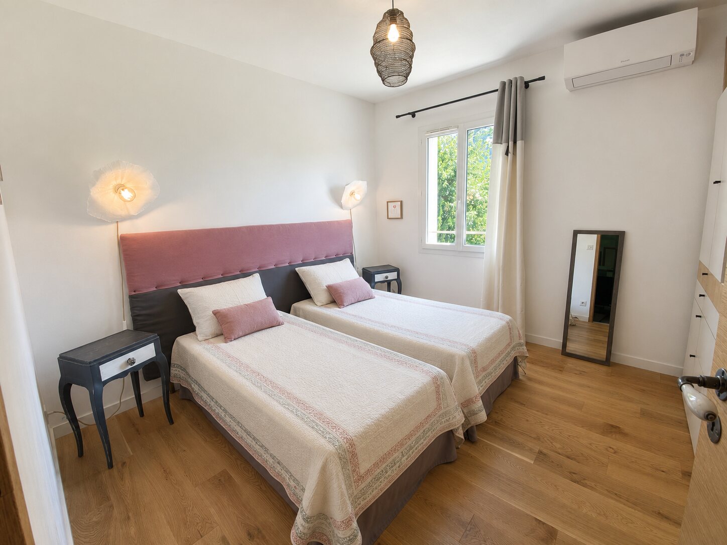 Chambre à deux lits aux nuances écrues et rose poudré avec vue sur le jardin